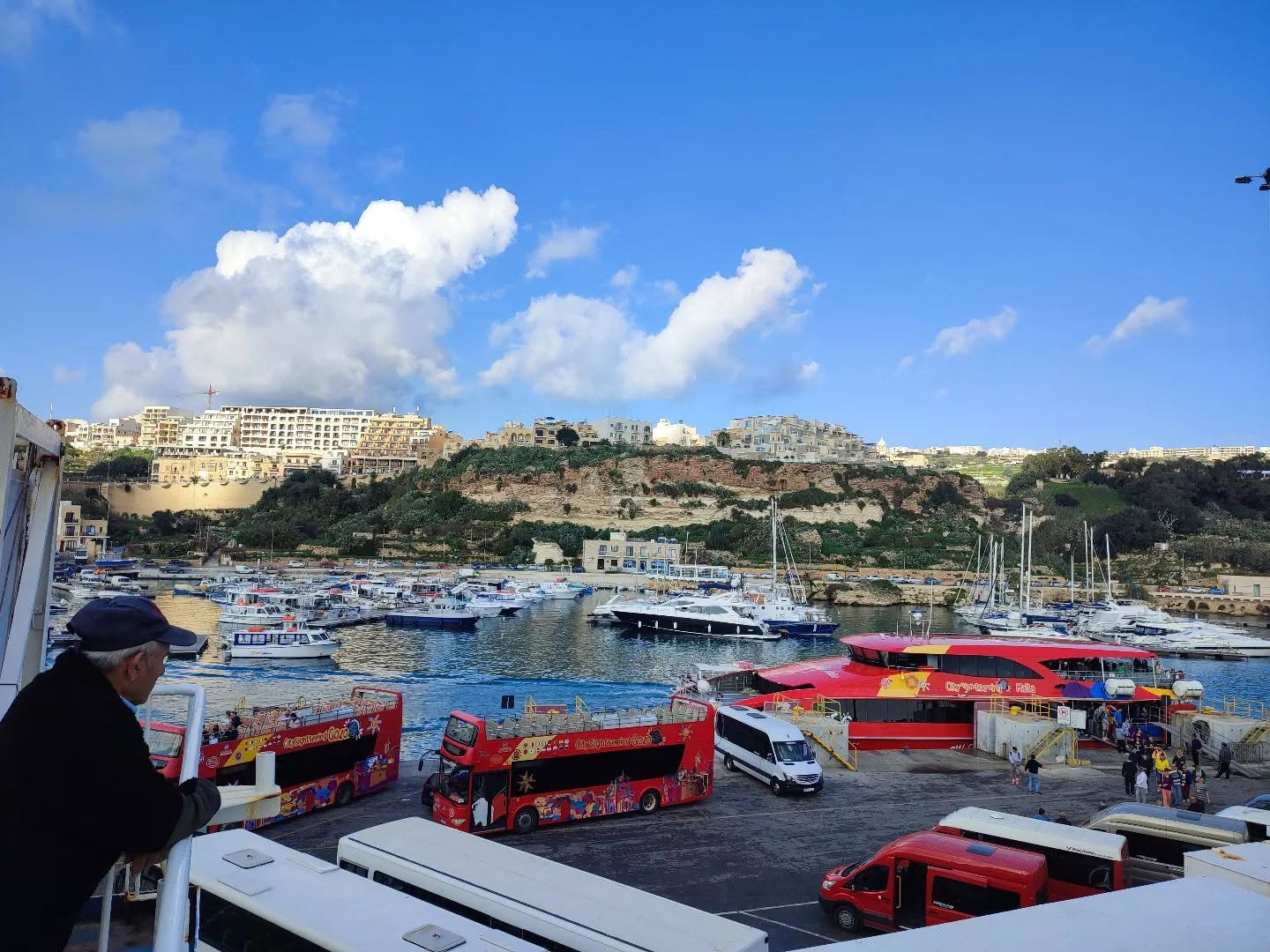 Gozo harbour with ferries, marina and hillside buildings under blue sky
